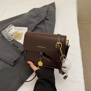 Detail of a deep brown crossbody bag with gold lettering and a plush monster charm