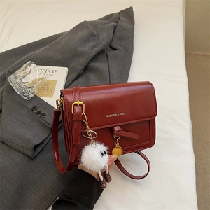 Detail of burgundy leather crossbody bag with fashion lettering and cute white plush charm