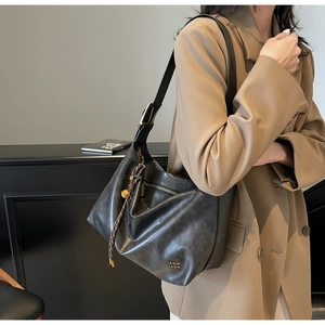 Close-up of black high-capacity tote bag featuring metal logo and weave charm decoration