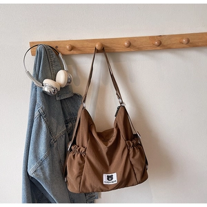 Close-up of brown canvas crossbody bag with Myron Bear patch and drawstring pockets
