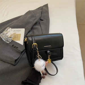 Detail of minimalist black crossbody bag with golden clasp and white pompom charm