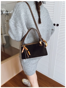 Détail du sac en daim noir avec bandoulière en cuir marron et pendentif à pompon perlé