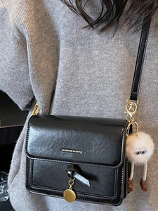 Minimalist black leather crossbody bag with chain and white plush charm on grey sweater