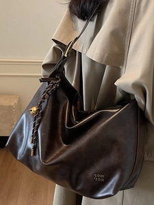 Minimalist large capacity dark brown leather tote bag with woven pendant on model shoulder