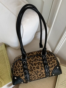 Retro leopard print bowling bag with black leather trim and silver metal eyelets on sofa