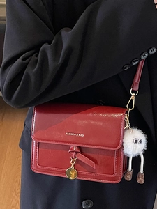 Chic red patent leather crossbody bag with chain and white plush charm on black suit