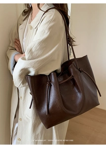 Detailed view of dark brown leather tote bag with drawstring knots and fine grain texture