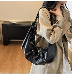 Detail of black pleated faux leather bag with adjustable ring buckle and knotted strap