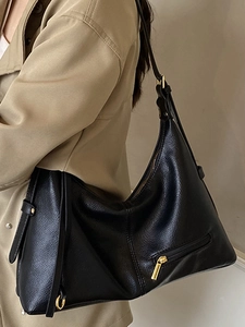 Stylish black leather tote bag with gold hardware worn over a beige trench coat