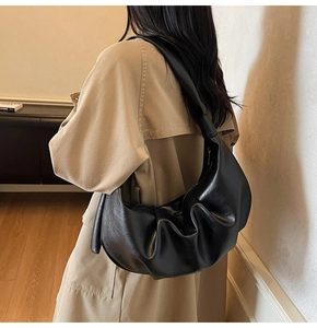 Detail of a black pleated slouchy dumpling bag worn on shoulder by a model