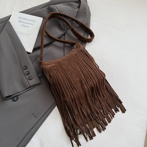 Détail d'un sac bandoulière en daim marron à franges avec une veste de blazer grise chic