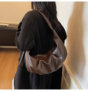 Detailed side view of a large brown pleated leather tote bag worn on a model's shoulder