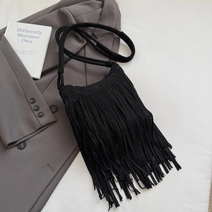 Détail d'un sac à bandoulière noir à franges en daim posé sur un blazer élégant