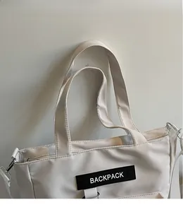 Détail d'un sac cabas beige clair en nylon lisse avec un écusson de logo noir
