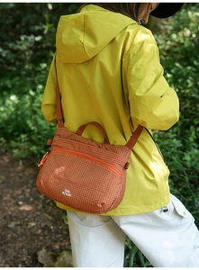 Detailed view of an orange checkered outdoor crossbody bag in a hiking forest setting
