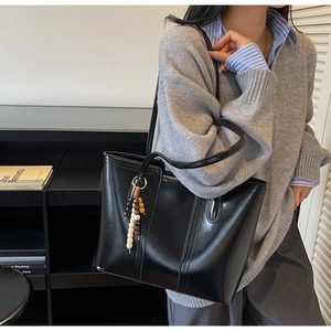 Close-up of black leather tote bag with wooden bead charm and sleek shoulder straps