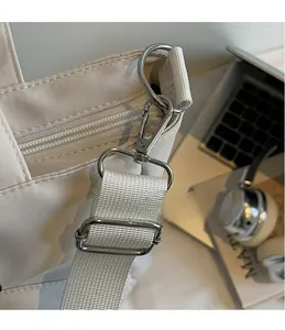 Détail du crochet en métal argenté et de la bandoulière tissée sur un sac en toile beige