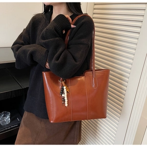 Detail of a deep brown tote bag with smooth texture and decorative beaded keychain pendant