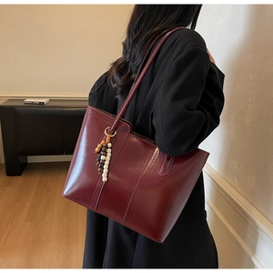 Detail of burgundy glossy leather tote bag with wooden bead charm on woman's shoulder