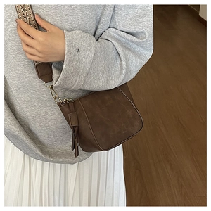 Detail of dark brown crossbody bag with ethnic pattern strap and tassel decoration