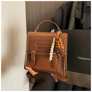 Dettaglio zaino in pelle intrecciata marrone con ciondolo in legno e fibbie metalliche