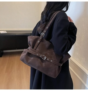 Detail of dark brown suede tote bag with silver buckle straps worn with a black coat