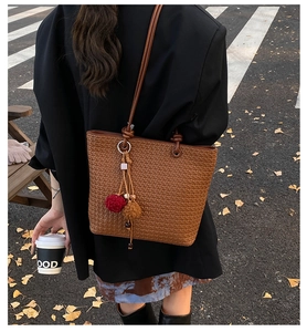 Brown woven tote bag detail with colorful pompom tassel pendant and textured surface