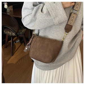 Close-up of brown matte shell bag with jacquard geometric strap in coffee shop setting