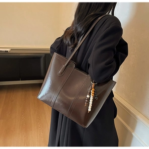 Detail view of large dark brown tote bag with retro wooden bead charm and leather texture