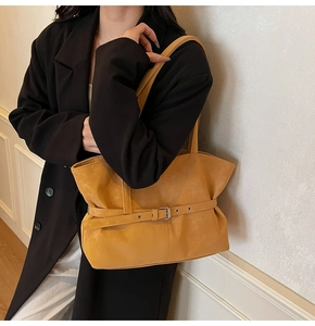 Detail of mustard yellow tote bag with metallic buckle strap and matte leather texture
