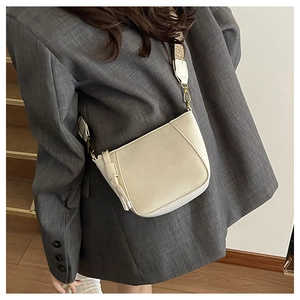 Detail of off-white shell bag with wide shoulder strap worn with a grey blazer