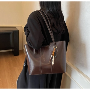 Detail of dark brown glossy tote bag featuring vintage beaded tassel charm and stitch detail