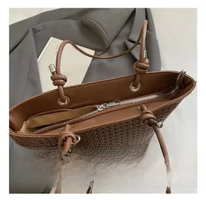 Close-up of woven dark brown tote bag showing smooth leather handles and metal zipper detail