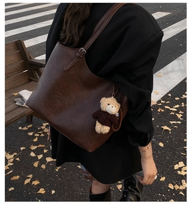 Detail of a large dark brown oil wax leather tote bag with a cute teddy bear charm