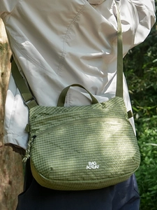 Dark green checkered crossbody bag with adjustable strap worn by a model in nature