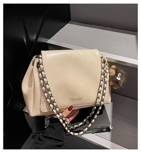 Detail of off-white leather tote bag featuring metal chain strap and plush monster charm