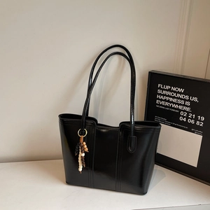 Close-up of black glossy tote bag with vertical seams and wooden beaded charm