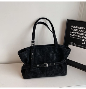 Detail of minimalist black suede tote bag with silver buckle strap on marble surface