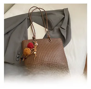 Detail of dark brown woven leather tote bag with colorful pompom charm on grey blazer