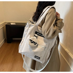 Détail du cabas en nylon blanc cassé montrant les poches zippées et le petit pendentif