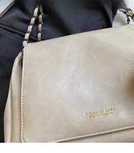 Close-up of cream chain bag featuring soft faux leather texture and gold logo detail