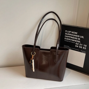 Detail of dark brown glossy tote bag with beaded pendant in minimalist interior setting