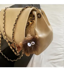 Detail of beige tote bag featuring a chain strap and a fuzzy brown monster charm