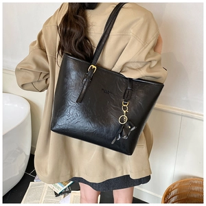 Detail view of large black glossy leather tote bag with elegant golden metal buckle and charms