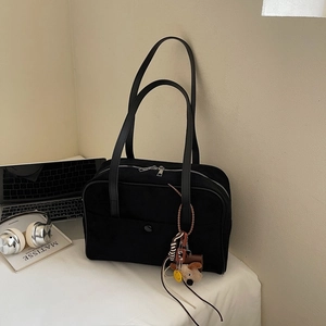 Detail of black suede bowling bag with dual zippers and plush dog charm on white desk