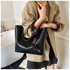 Minimalist black large capacity tote bag with leaf pendant charm worn with a trench coat