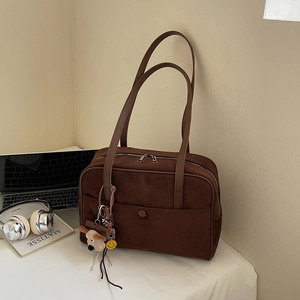 Close-up of brown suede hobo bag with top zipper and cute puppy charm on desk