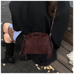 Detail of vintage burgundy suede crossbody bag with long side tassels in outdoor setting
