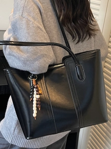 Large black tote bag in glossy leather with wooden bead tassel charm on a model's shoulder