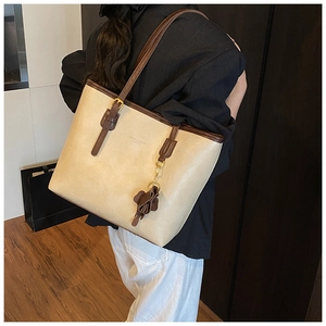 Detailed view of a beige tote bag with brown trim and floral charm worn by a model